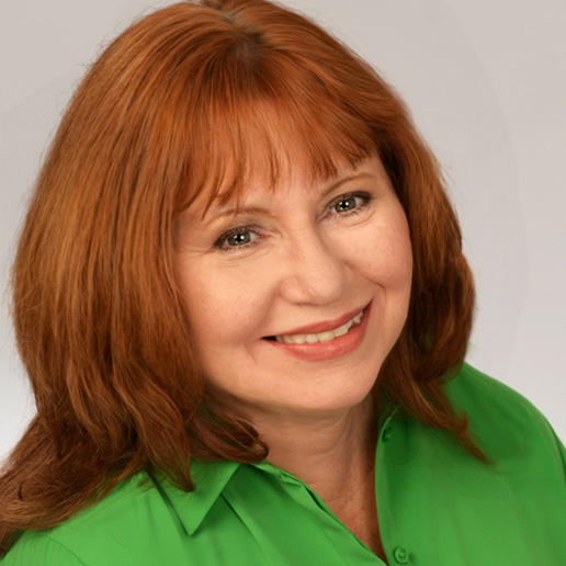 A woman with straight, shoulder-length red hair and bangs smiles warmly. She is wearing a bright green collared shirt and is posed in front of a plain, light-colored background.